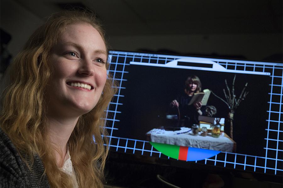 A student sits next to her work displayed on a computer.