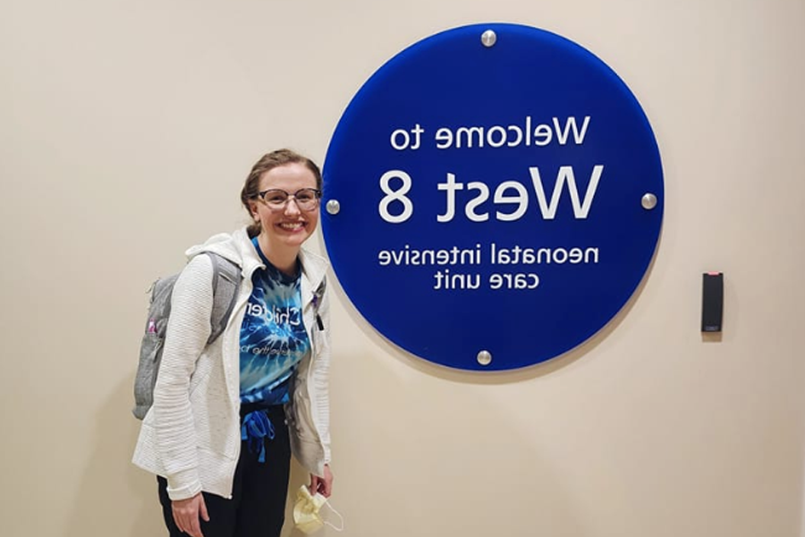 Keeley O'Dell poses by a sign that says Welcome to West 8 neonatal intensive care unit.