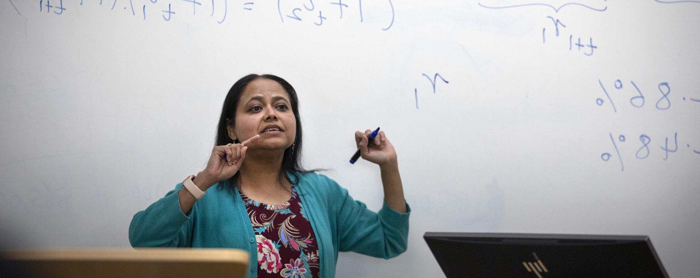 A faculty member teaches in front of a whiteboard.